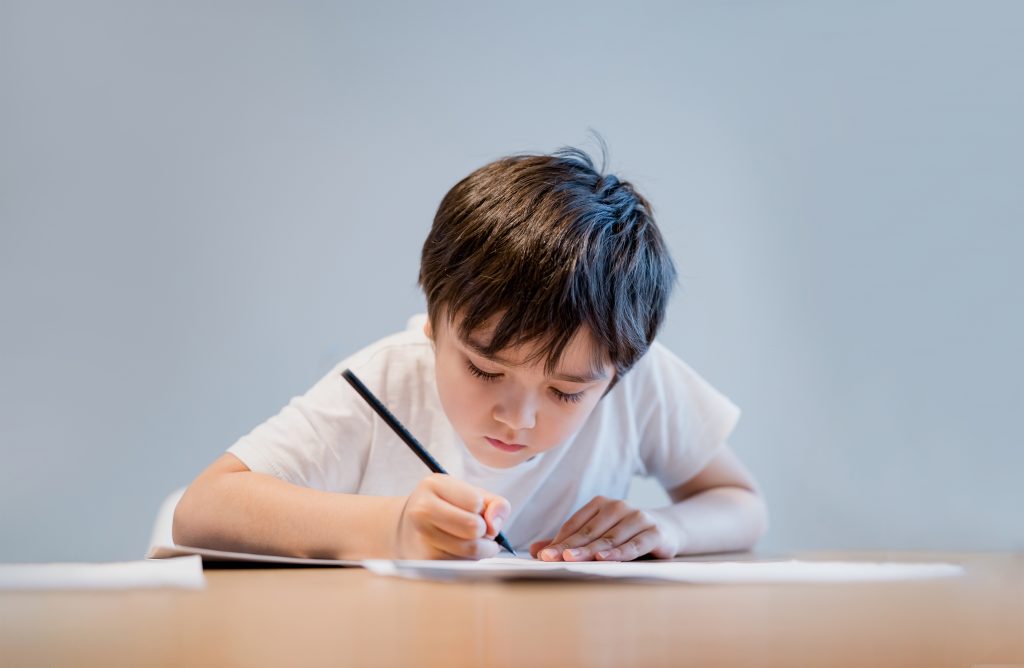 Kid holding pencil writing on white paper, Child boy is drawing.school kid doing homework